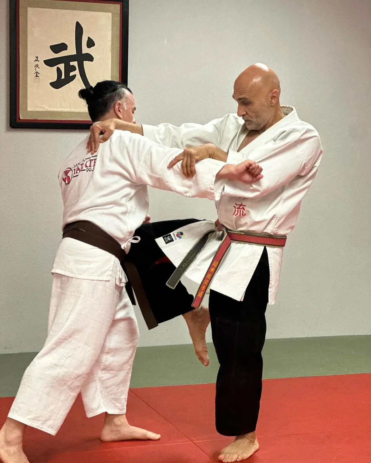 Adults practicing a karate partner drill on the red mats at Samurai Dojo
